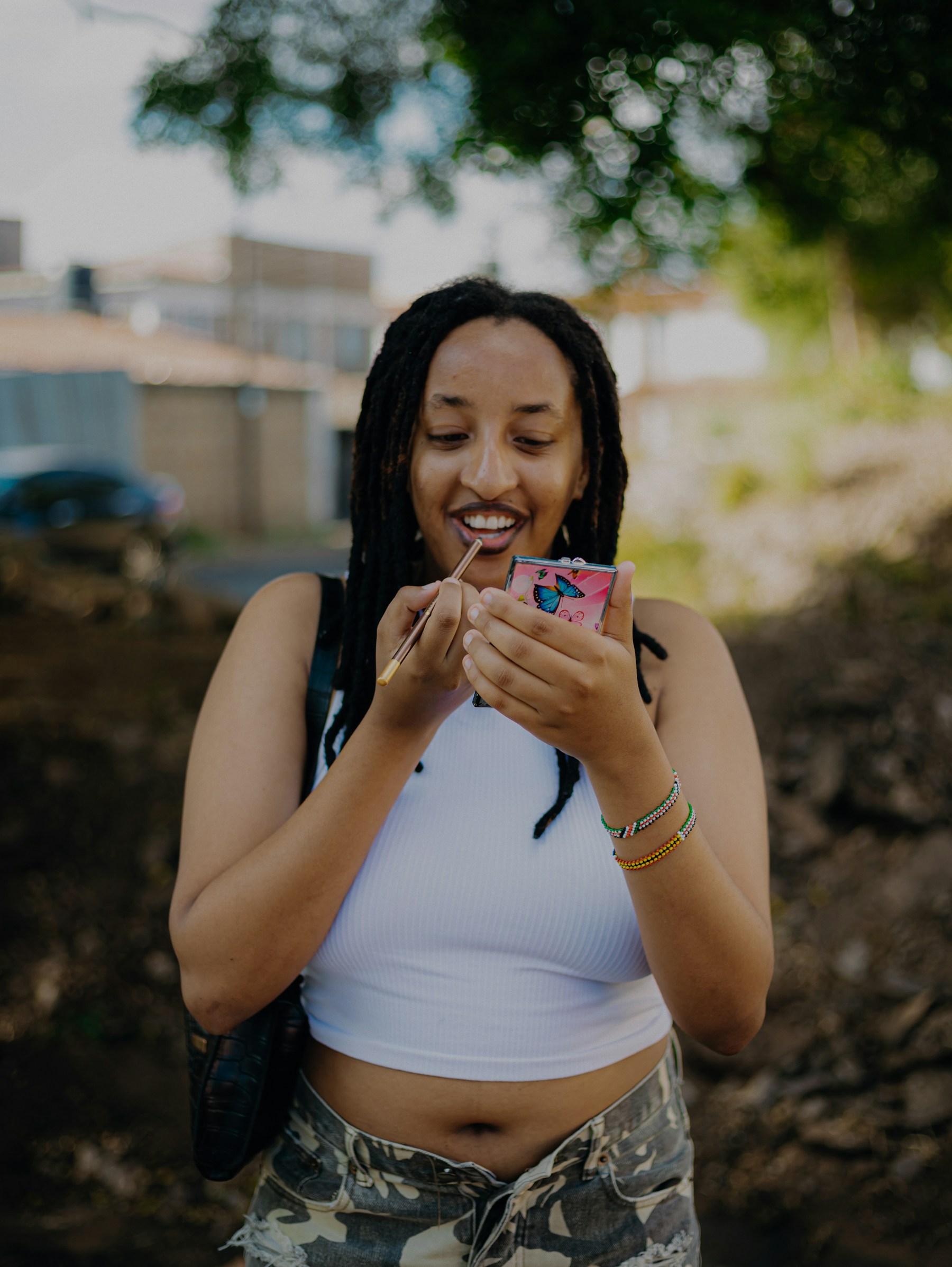 Woman applying lipstick from compact mirror outdoors