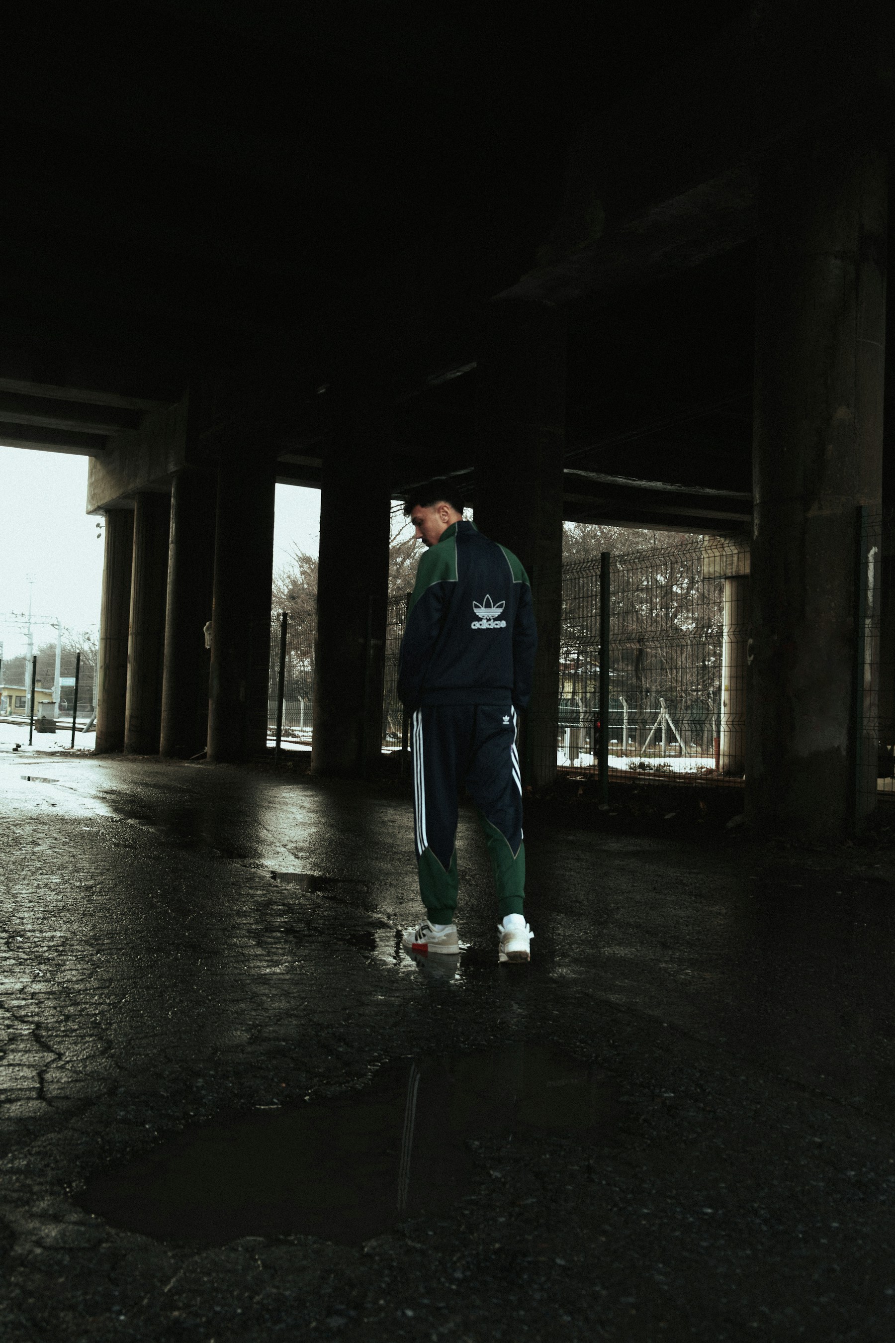 Man in tracksuit stands under concrete structure
