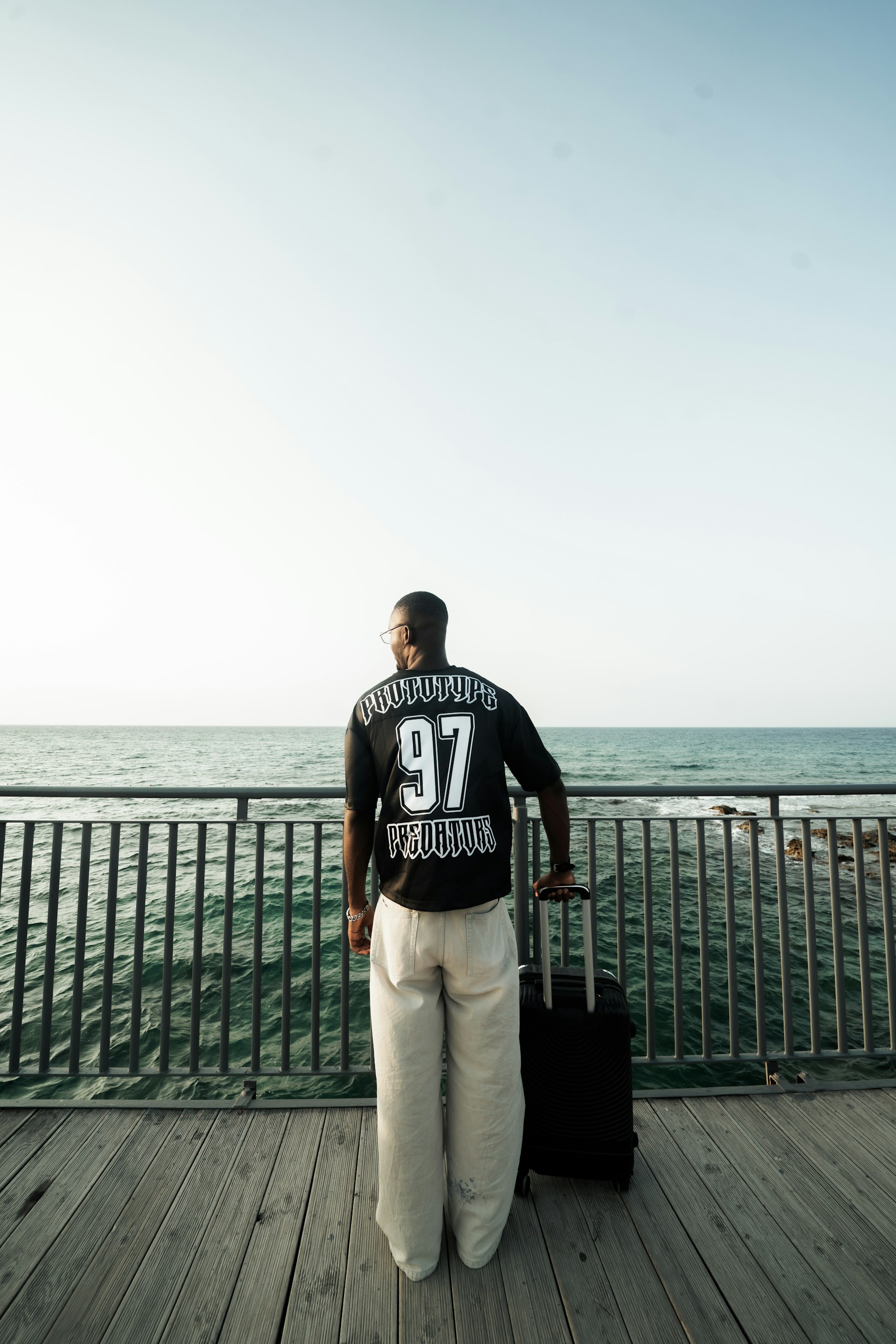 Man with suitcase on pier overlooking the ocean.